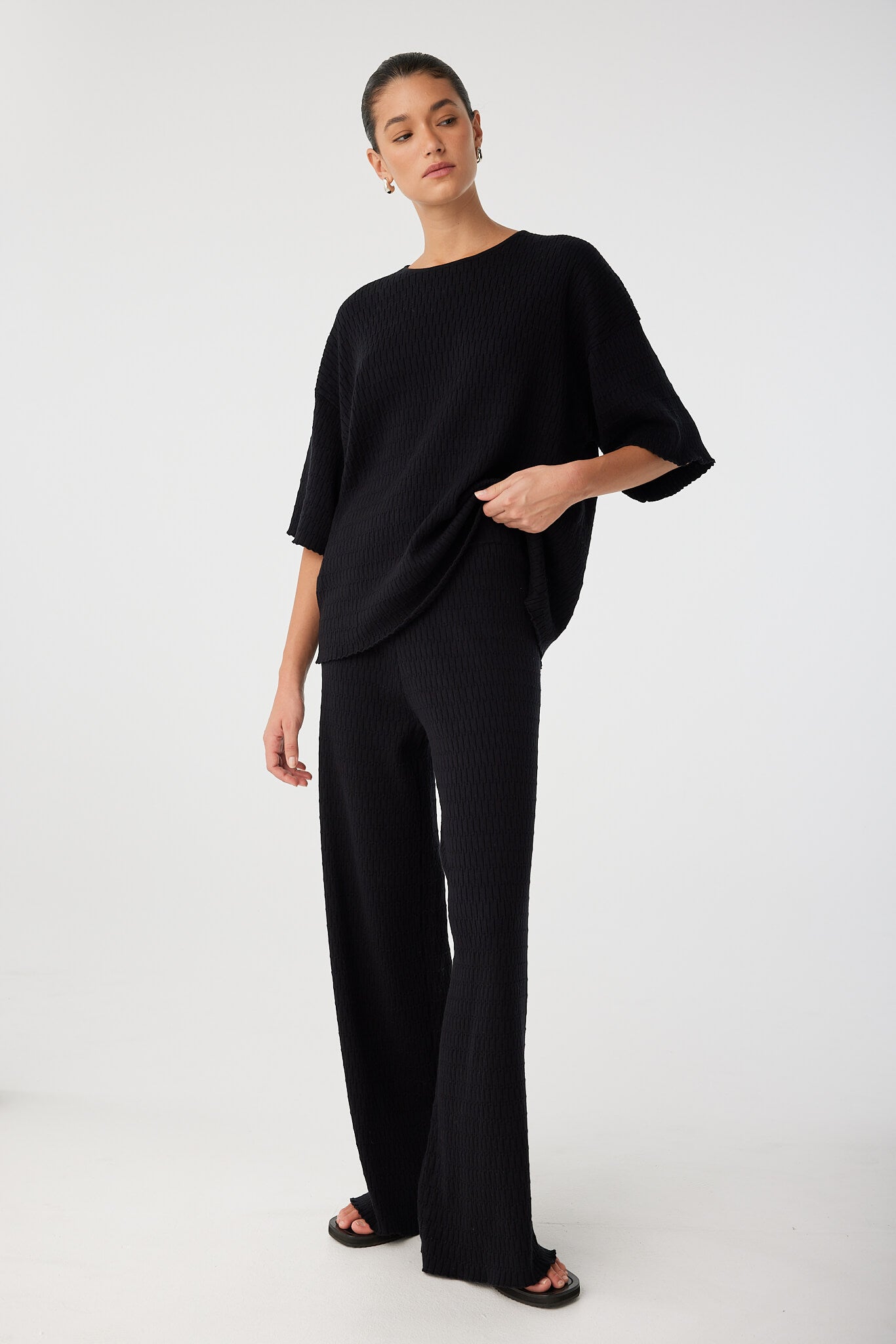 Side view of model wearing black textured knit pant styled with oversized black T-shirt.