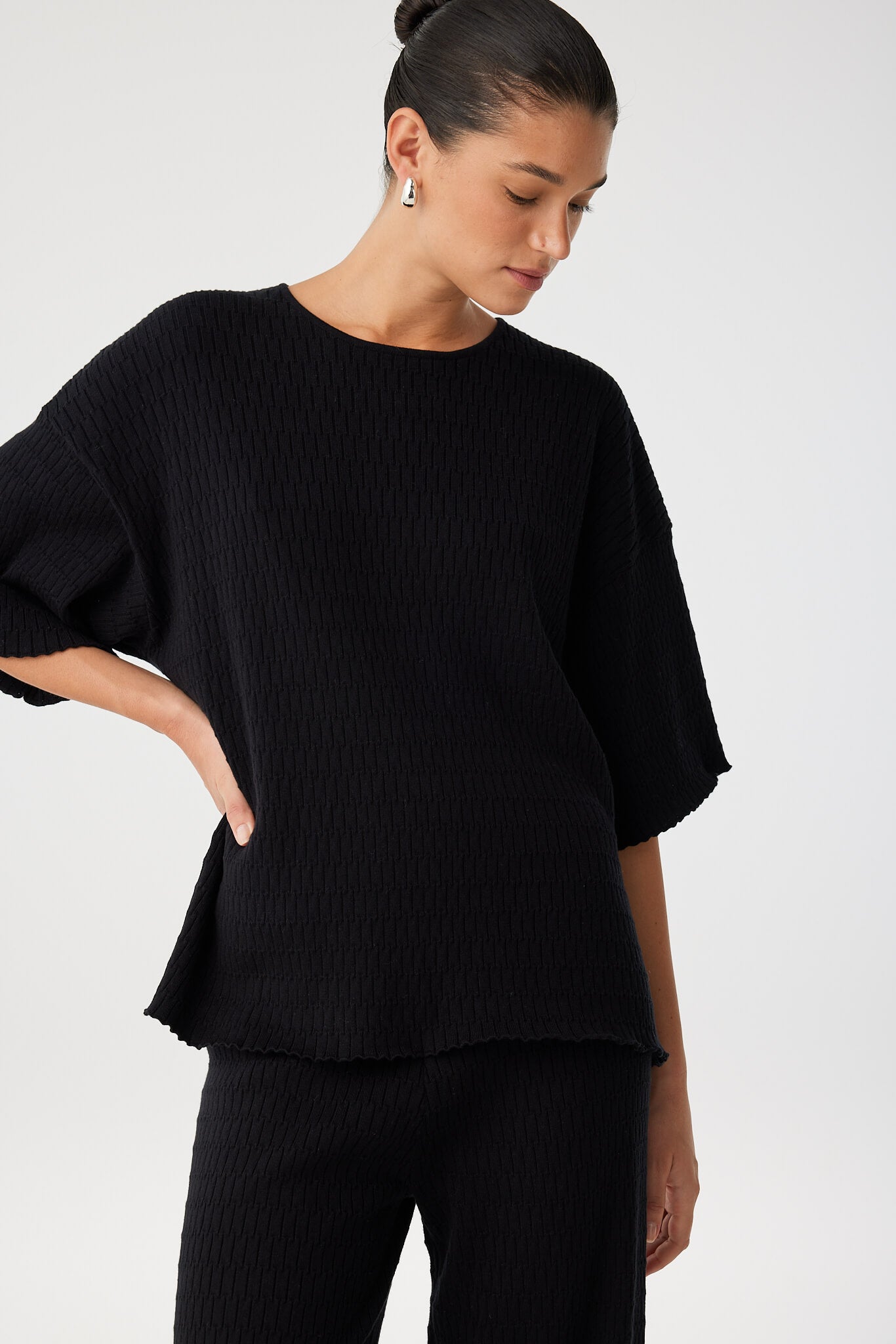 Side profile of model wearing oversized textured knit T-shirt in black with matching pants.