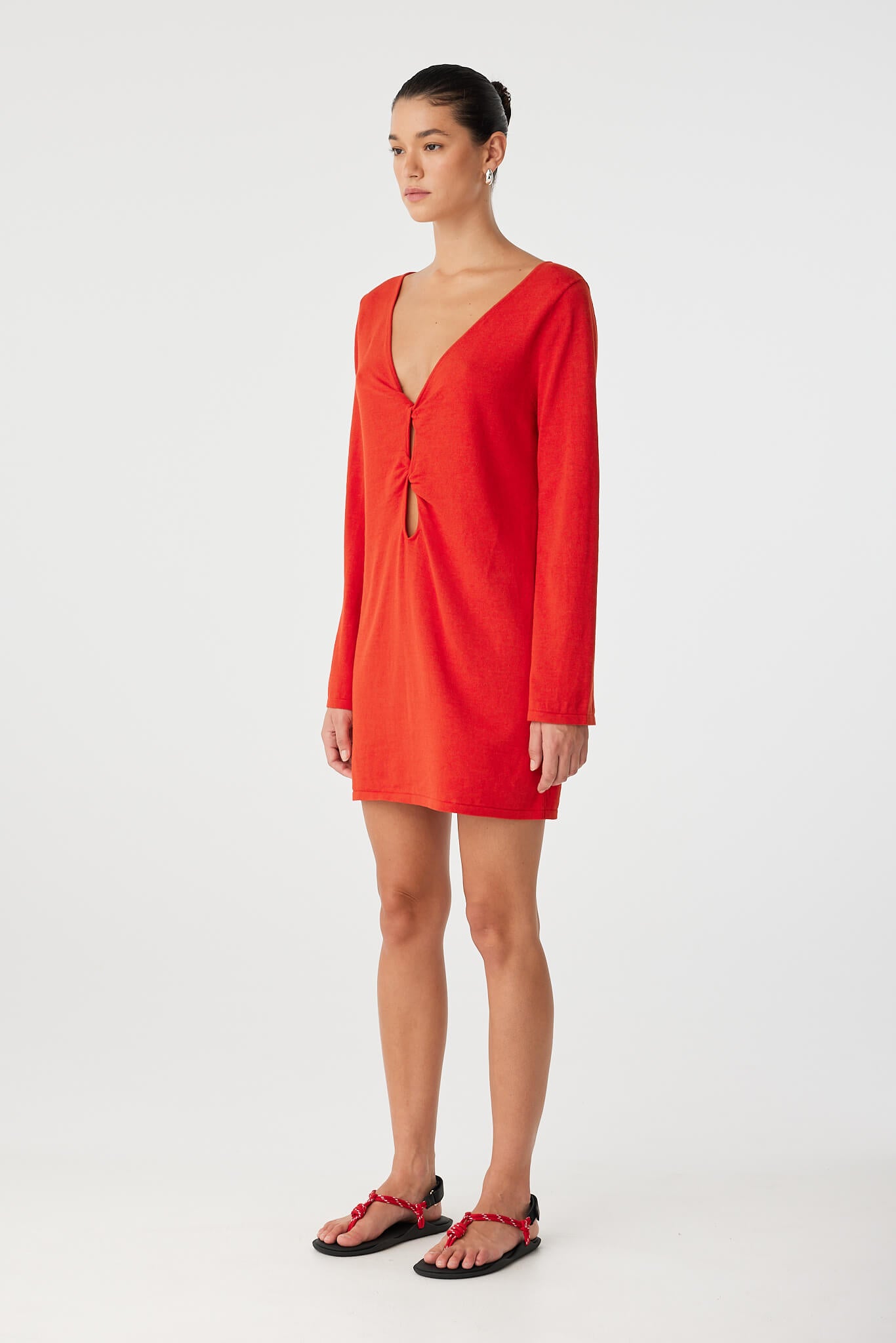 Side view of long sleeve mini dress in cherry red linen–cotton blend with deep V neckline and sculptural twist detail.