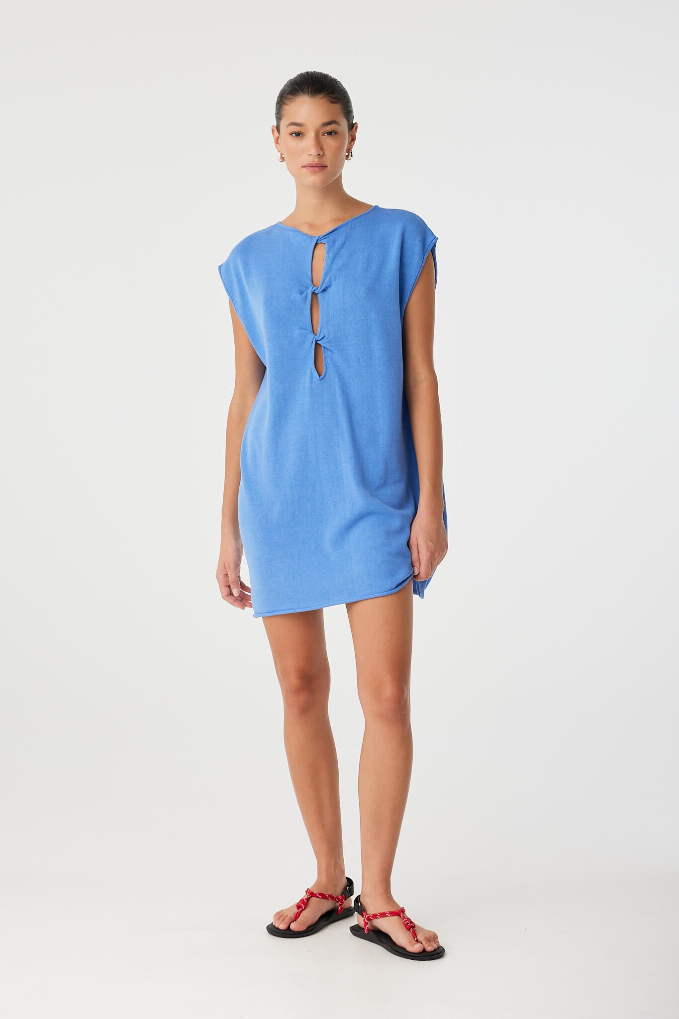 Model stands front-facing in pacific blue shift dress with twist detail worn at front, showing structured yet fluid fit in a breathable linen–cotton blend.