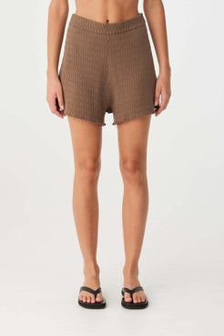 Model in minimalist cacao knit shorts with a wide rib waist and soft drape, ideal for warm-weather comfort.