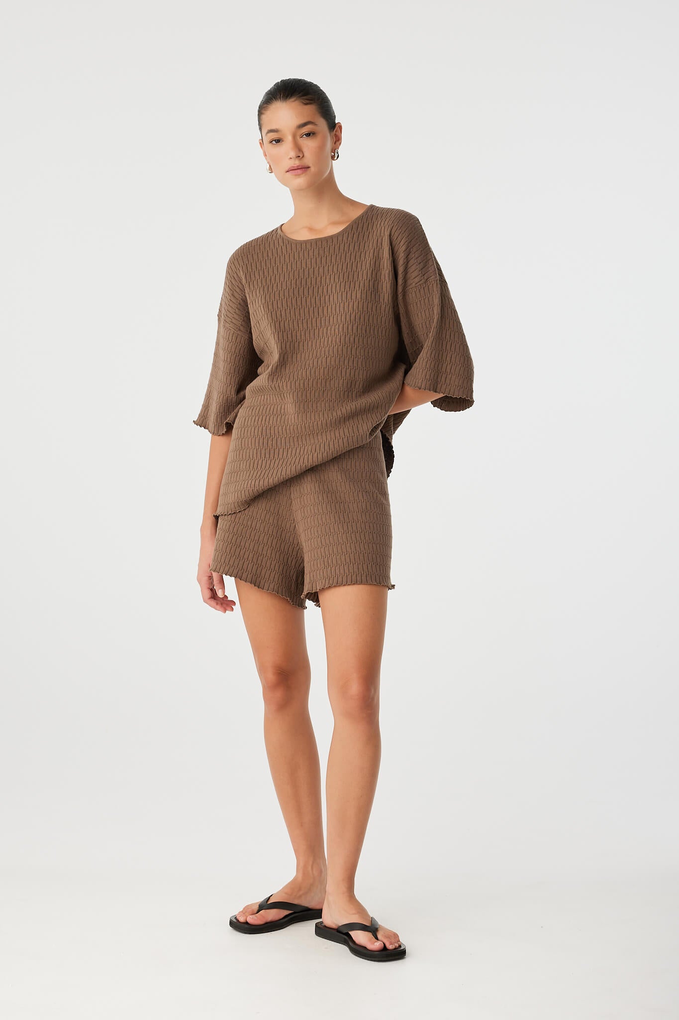 Model wears sculptural textured tee with one side tucked, showing flexibility in styling and drape.
