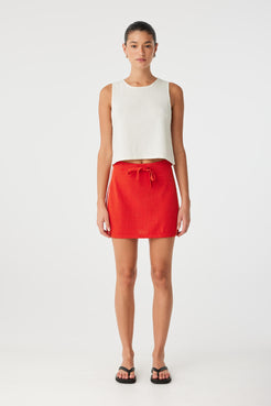 Model in ribbed knit tank with relaxed silhouette and rolled neckline, paired with drawstring mini skirt for warm-weather styling.