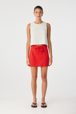 Model wears cherry red mini skirt with ribbed waistband and white contrast side stripes—styled casually for summer ease.