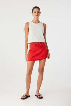 Relaxed-fit red skirt styled casually with white ribbed tank, showing subtle texture and side contrast detail.