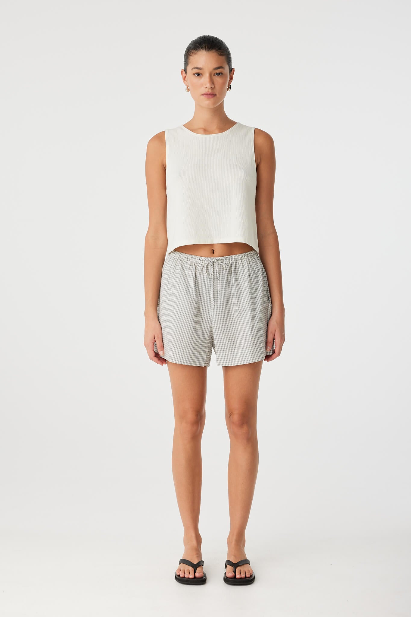 Model wears relaxed-fit cotton shorts in black check with drawstring waist, styled for warm days or coordinated layering.