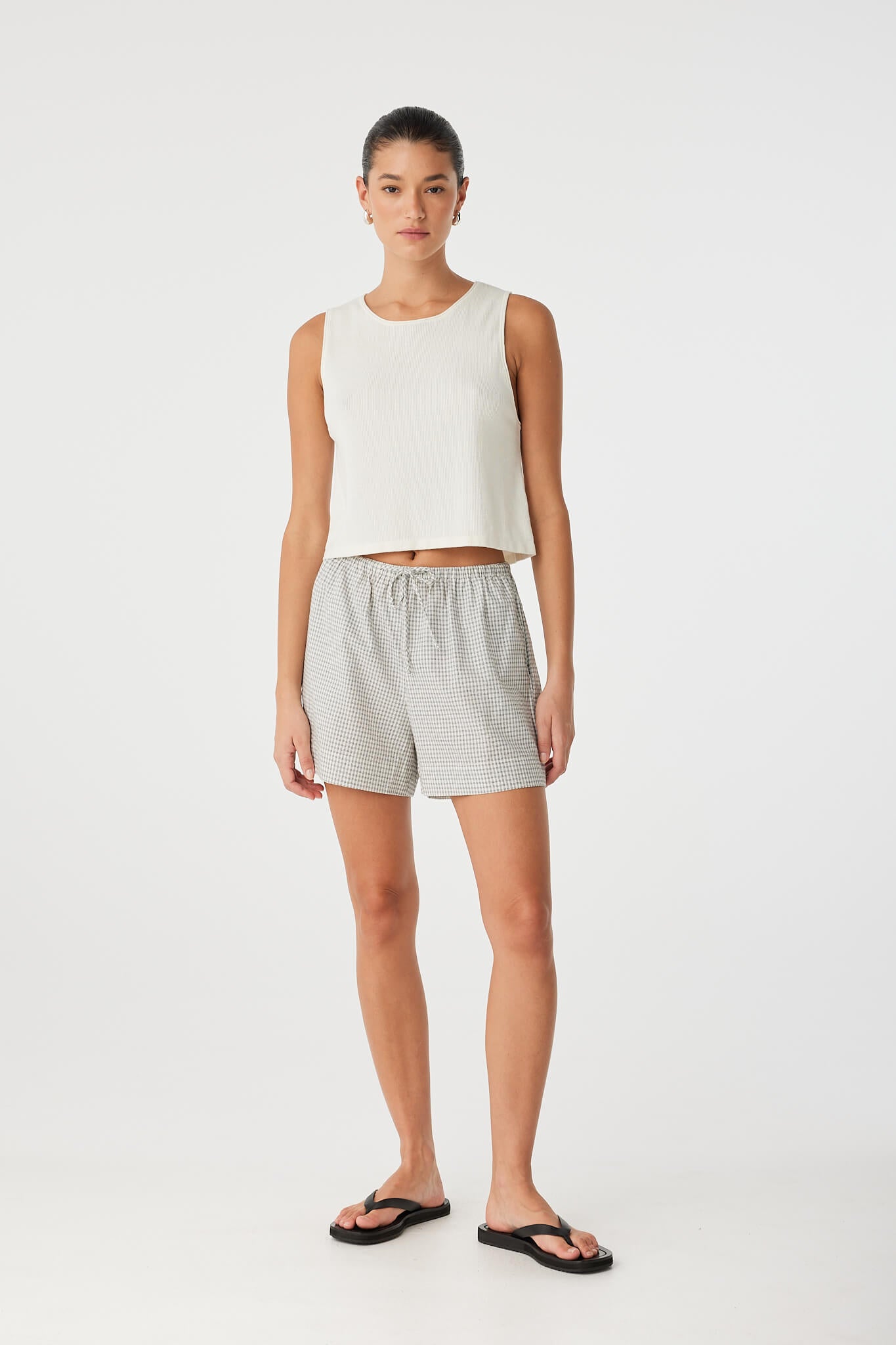 Model wears relaxed-fit drawstring shorts in lightweight black check cotton, styled with a ribbed tank for warm-weather comfort and minimal layering.