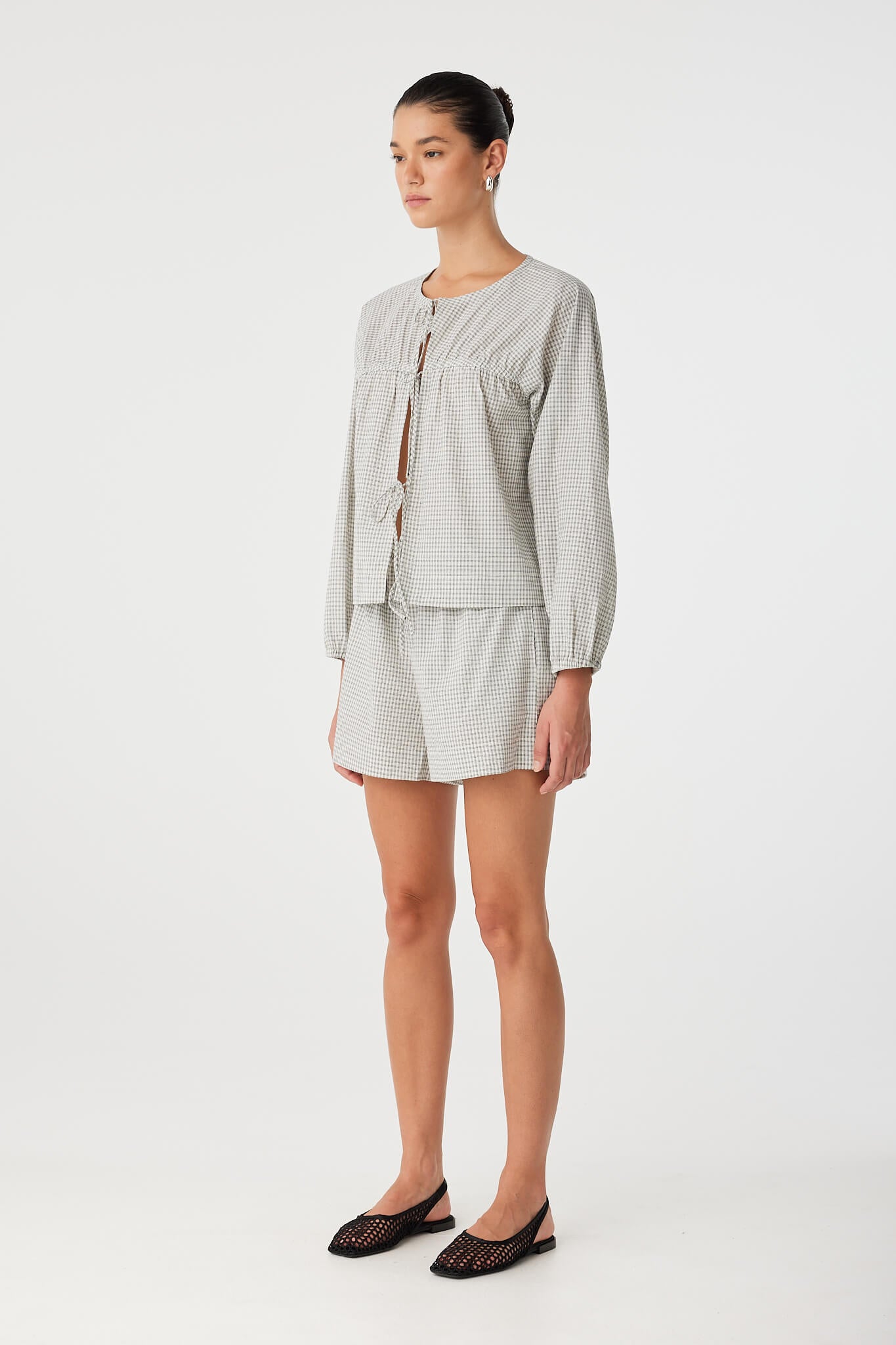 Side view of tie-front blouse with subtle volume in sleeves, layered over black check shorts for warm-weather ease.