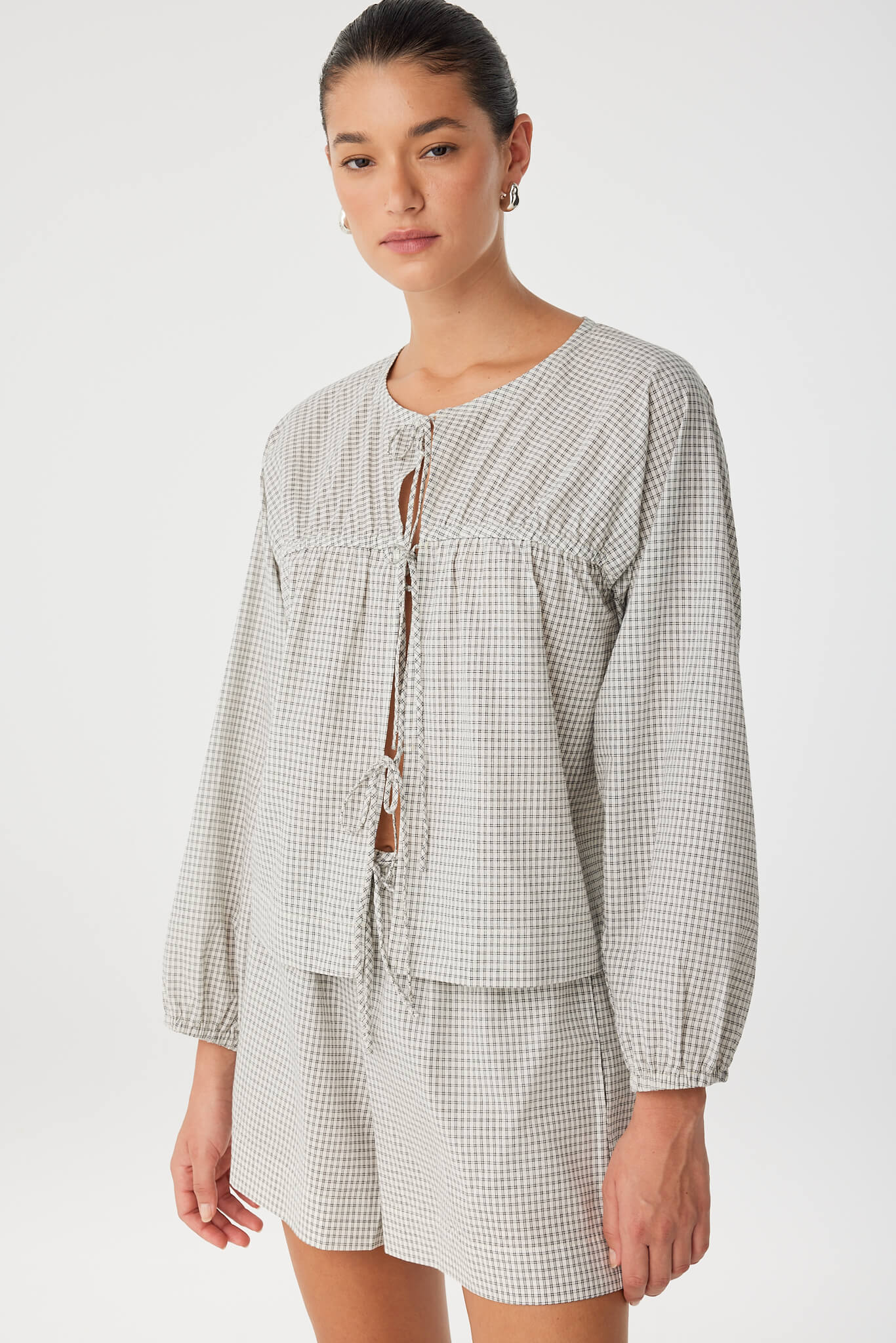 Model in softly structured blouse with long sleeves and front tie closure, styled in matching black check set.