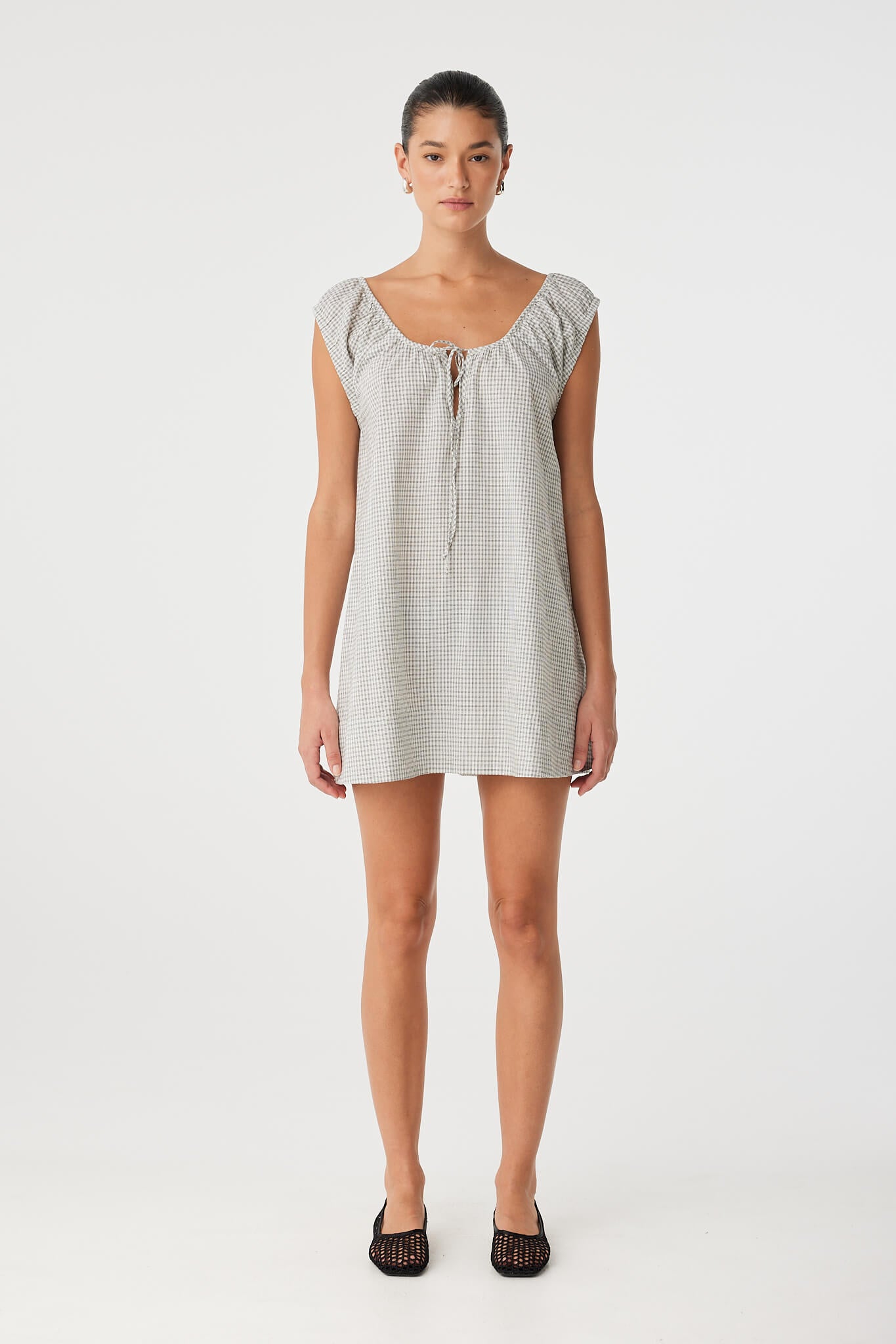 Model wears a relaxed-fit mini dress in lightweight black check cotton with flared hem and drawstring neckline—ideal for warm-weather comfort.