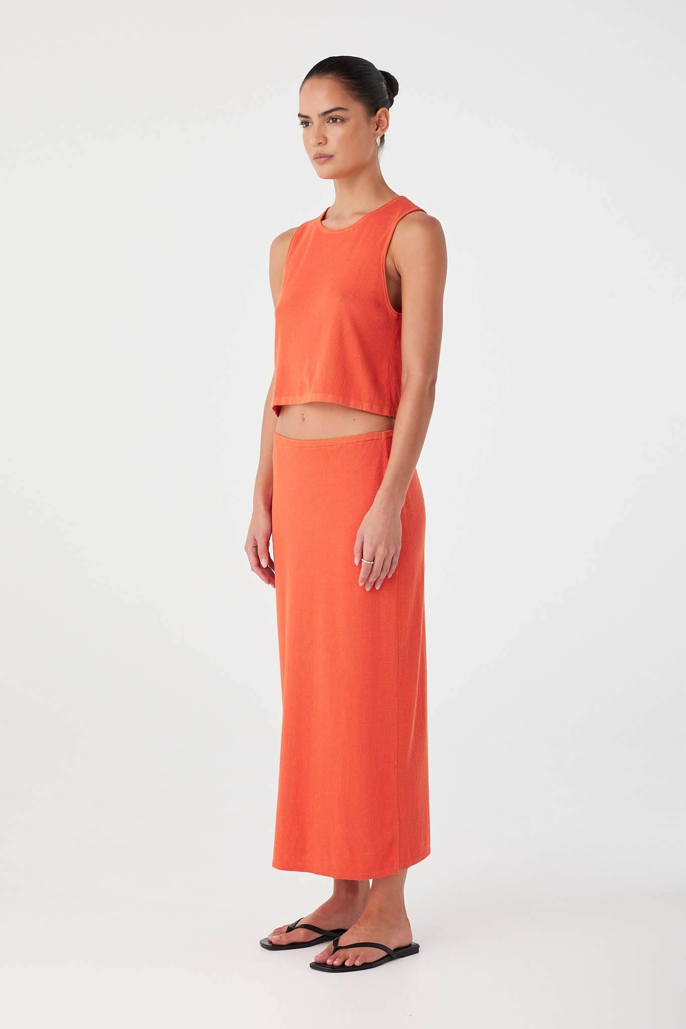 Side profile of orange (mandarin) rib knit skirt with soft drape and concealed elastic waistband.