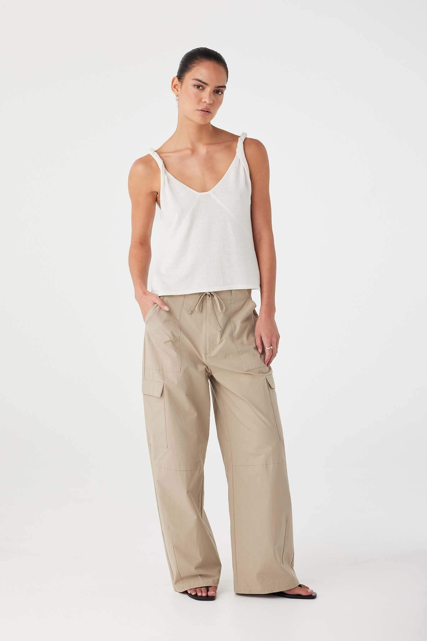 Model in cream V-neck tank with twist straps and shaping seams, paired with wide-leg cotton pants for effortless warm-weather wear.
