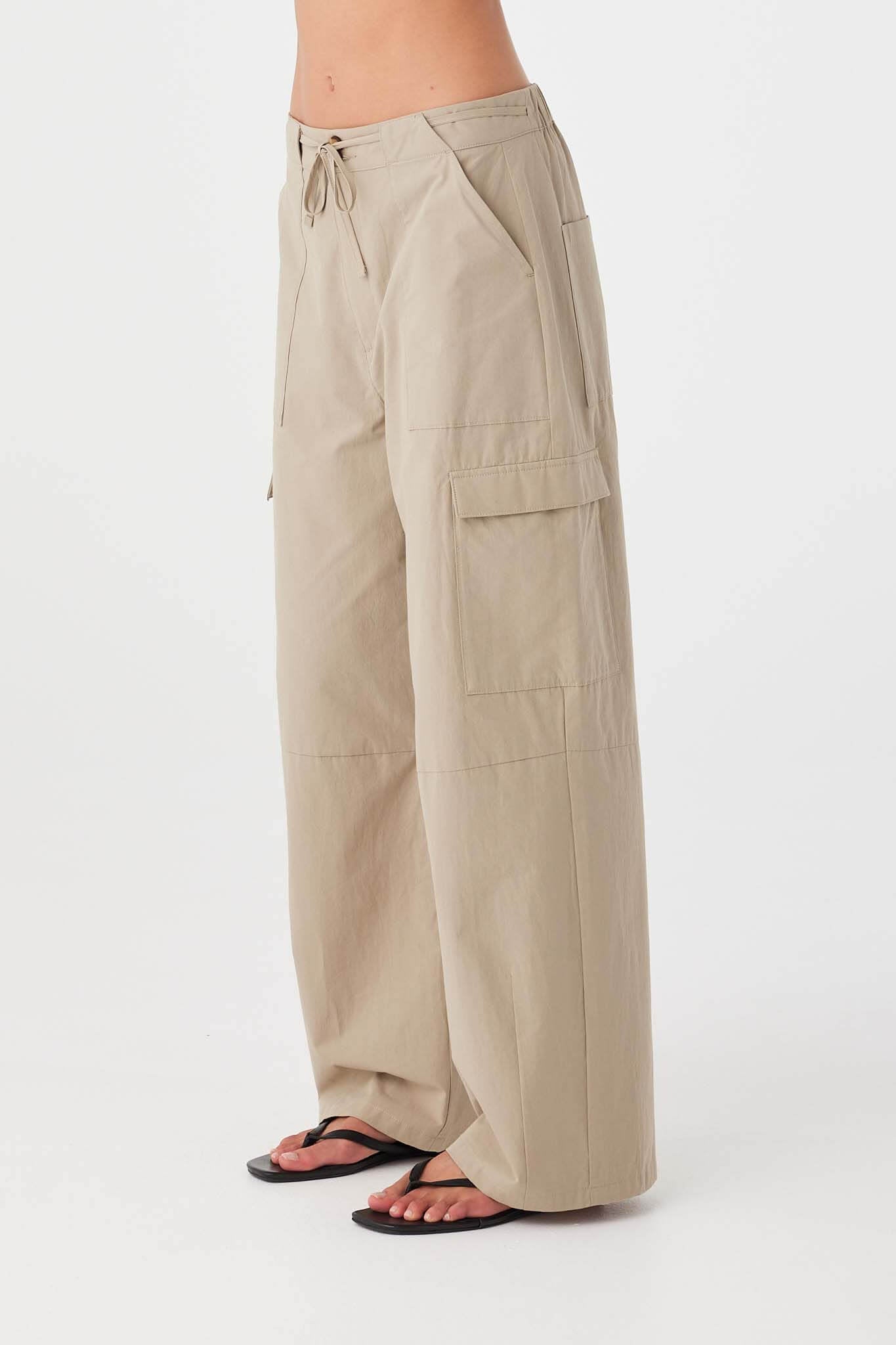 Taupe cotton pants with gentle barrel leg and functional side patch pockets, falling softly to the ankle.