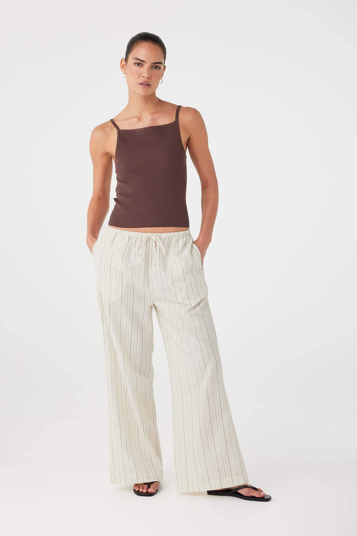 Model in olive stripe cotton drawstring pants styled with brown tank top for warm-weather ease.