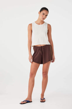 Model in espresso linen cotton drawstring shorts styled with cream tank, designed for lightweight summer wear.