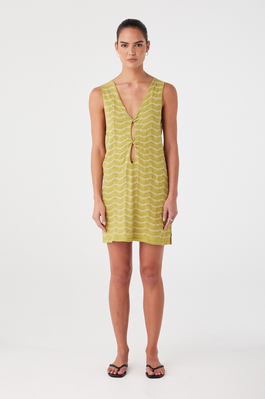 Model wears relaxed mini dress in wave-textured knit. Matcha green linen–cotton blend with twist cutout detail and sleeveless shape.
