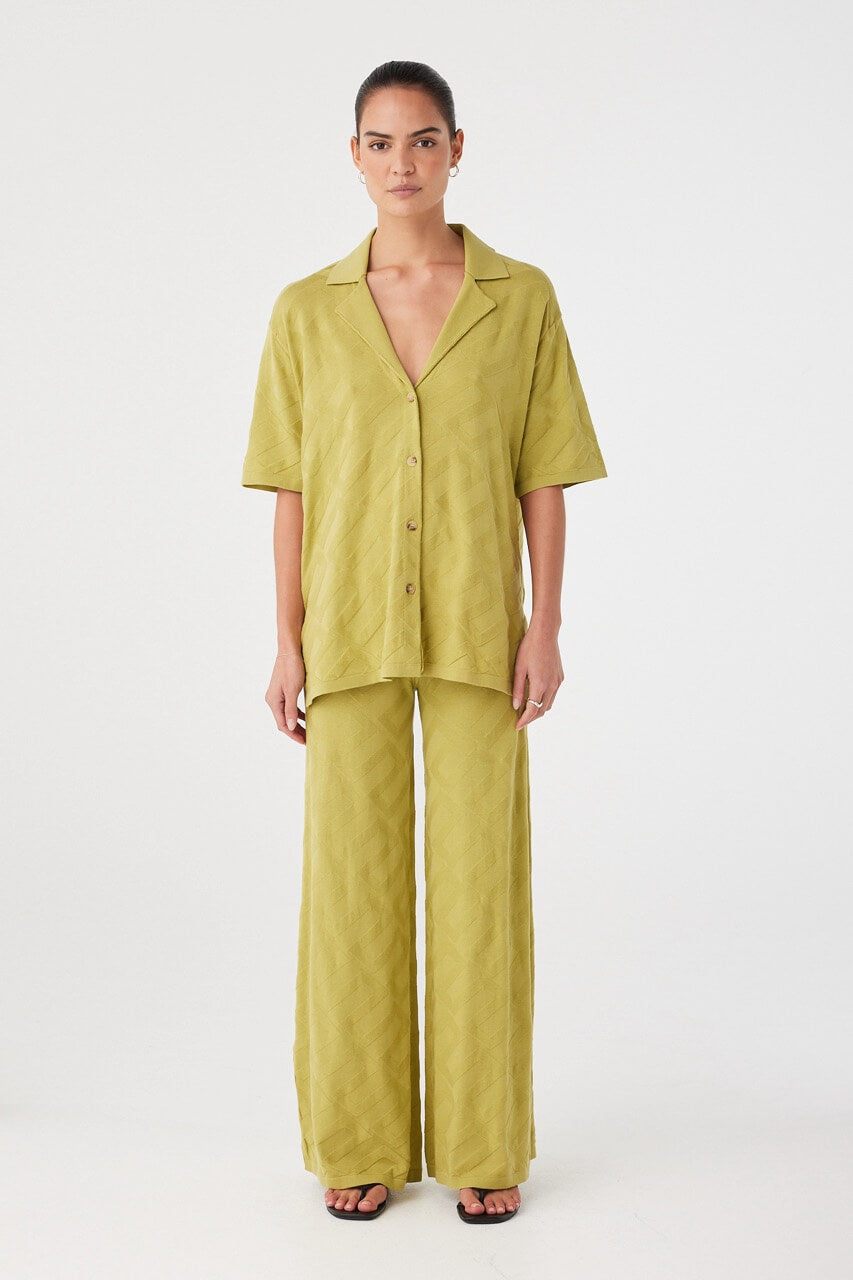 Model wears full-length pants in matcha green organic cotton knit. Wide-leg silhouette with soft drape and breathable texture.