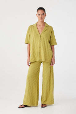 Model wears matcha oversized shirt with wide-leg pants. Lightweight organic cotton and tonal texture designed for trans-seasonal dressing.