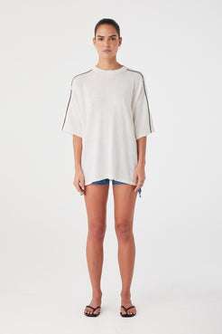 Relaxed oversized tee in cream with contrast stripe detail. Styled casually over shorts for lightweight summer layering.