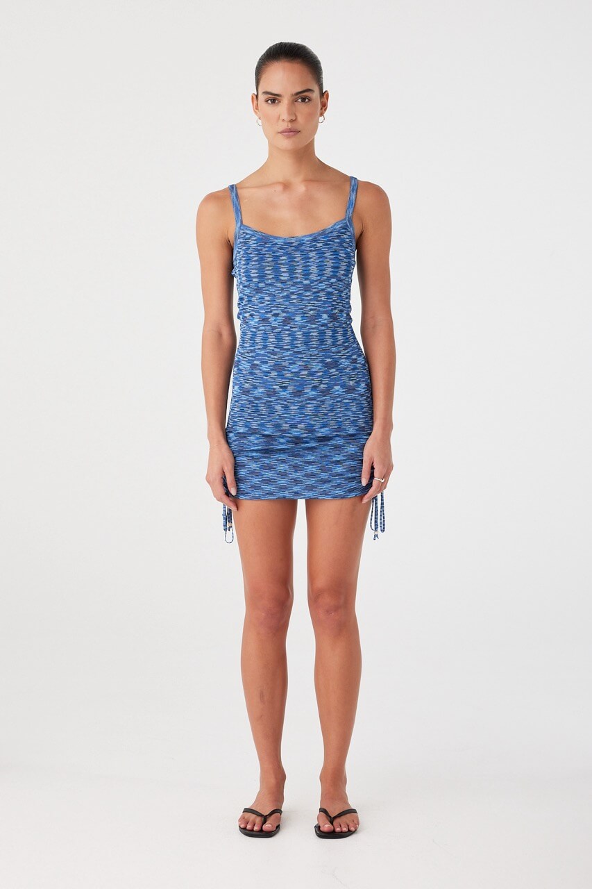 Model wears a fitted crochet mini dress in lapis blue with adjustable side ties and scoop neckline. Ideal for warm-weather layering or swim cover-up.