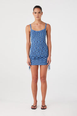 Model wears a fitted crochet mini dress in lapis blue with adjustable side ties and scoop neckline. Ideal for warm-weather layering or swim cover-up.
