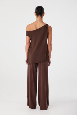 Back view of brown cotton knit asymmetric top with longline silhouette and off-shoulder neckline.
