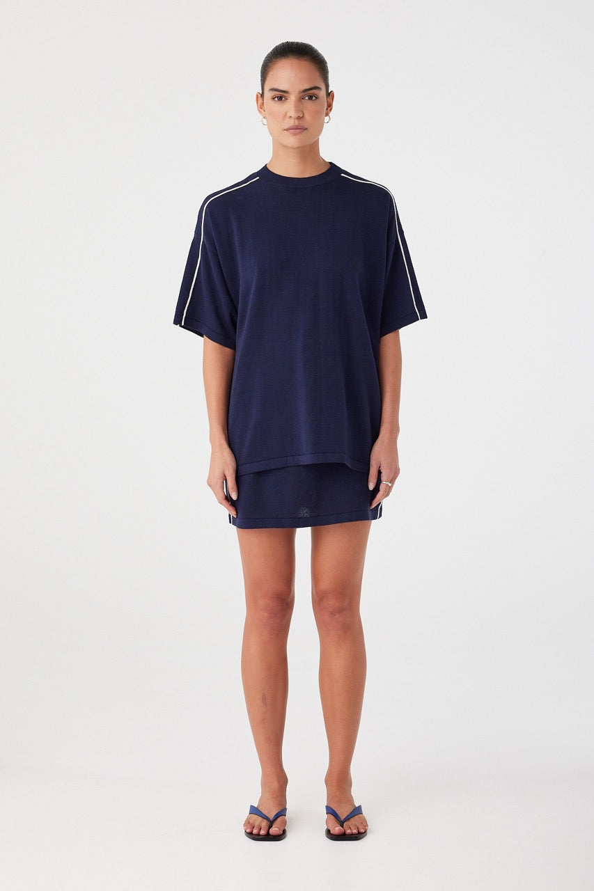 Oversized navy knit tee styled over mini skirt. Breathable texture and contrast stripe for elevated casual wear.