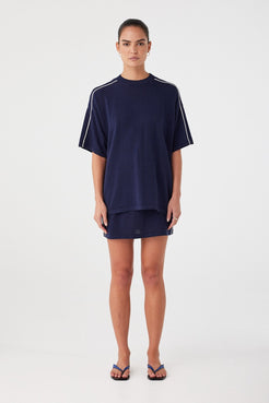 Oversized navy knit tee styled over mini skirt. Breathable texture and contrast stripe for elevated casual wear.