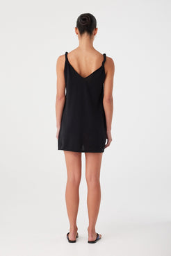 Back view of black linen blend mini dress with low scoop and twist strap detail. Easy movement and airy feel for warm days.