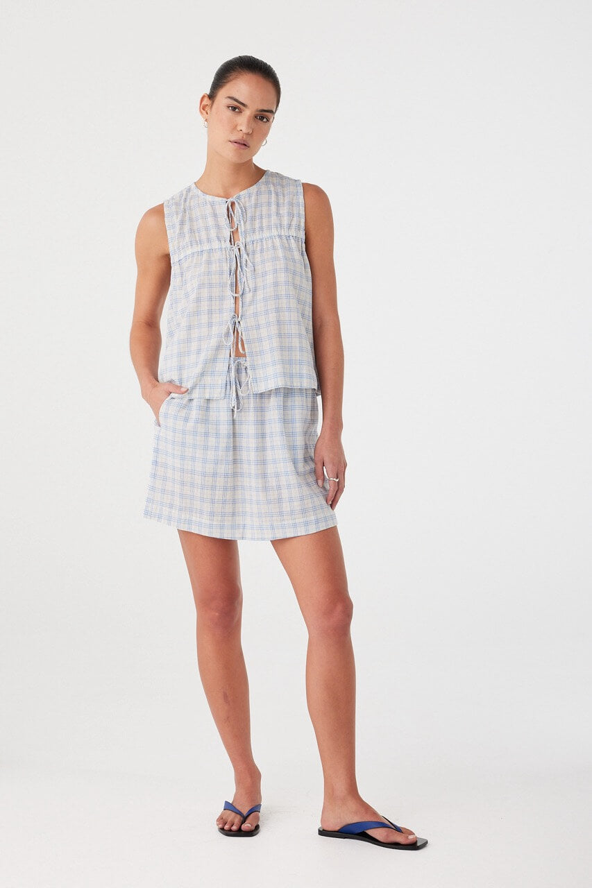 Model styled in full matching set. Tie-front blouse in blue cotton check with gathered detailing and lightweight finish.