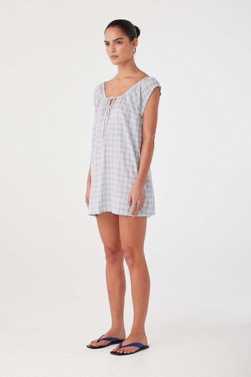 Side profile of flared mini dress in powder blue check. Adjustable neckline and lightweight texture for warm-weather ease.
