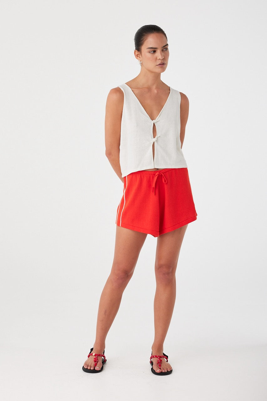 Woman wearing a white sleeveless top and red shorts on a white background