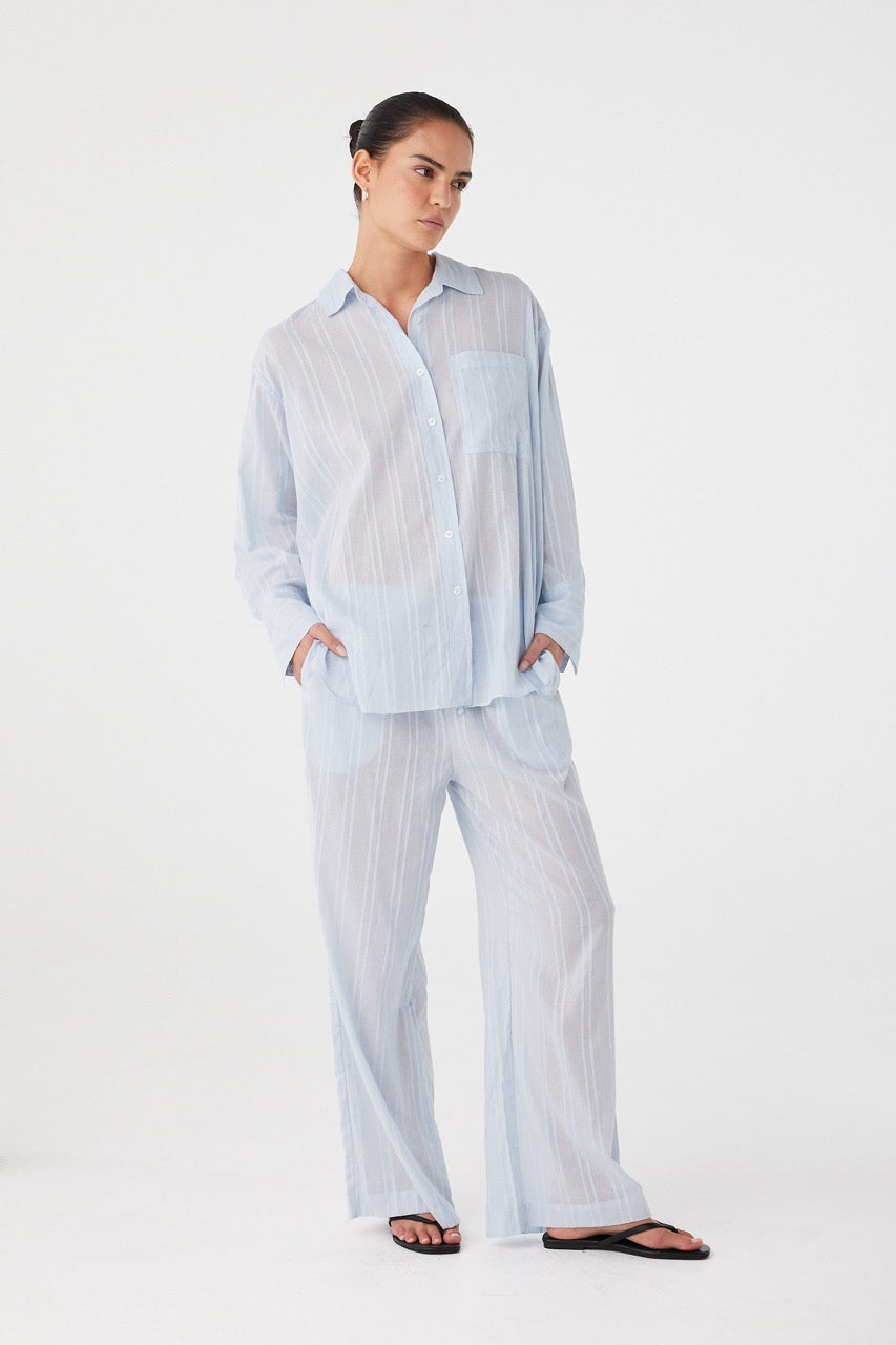 Model wearing matching oversized shirt and drawstring pant set in powder blue textured cotton; relaxed fit designed for effortless warm-weather layering.