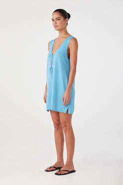 Side profile of a sleeveless cyan mini dress with soft drape and natural texture