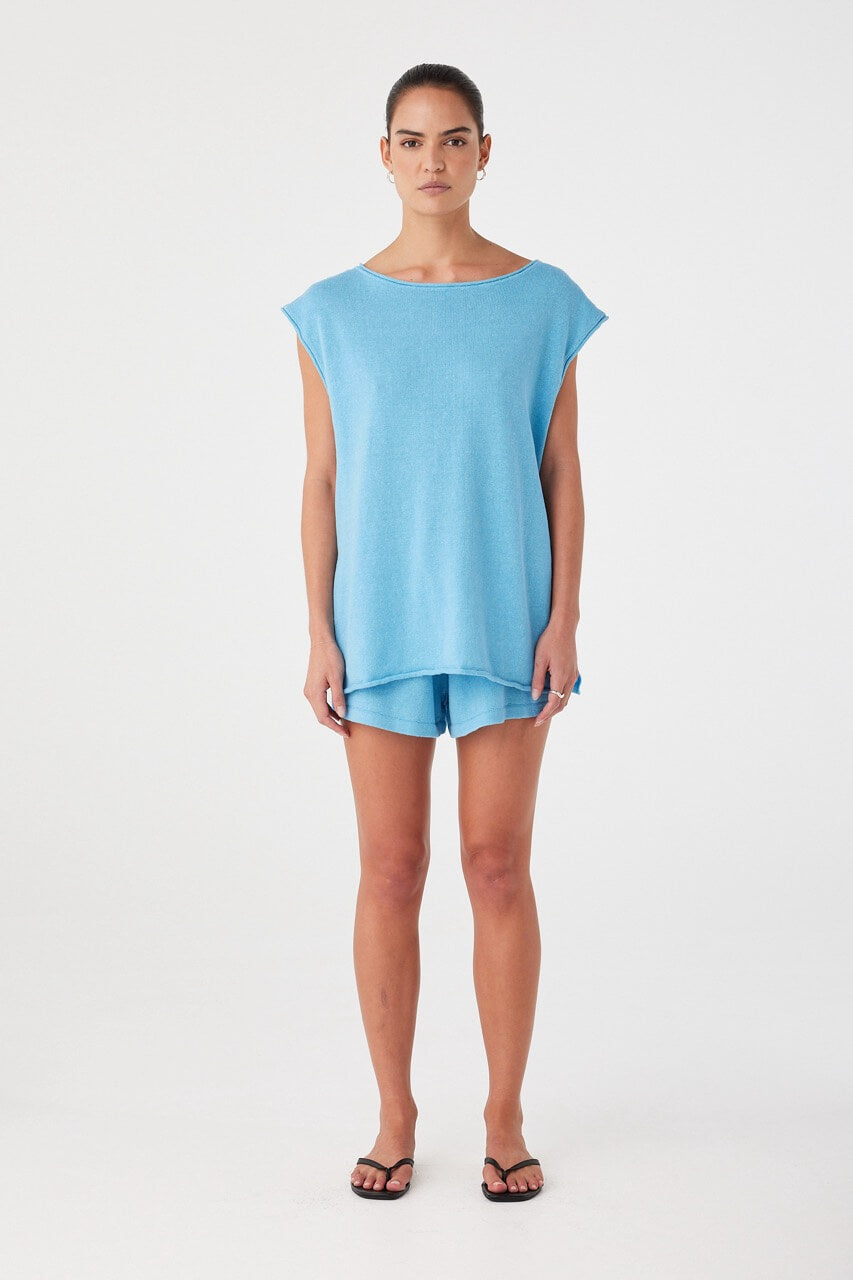 Model wears relaxed-fit linen-cotton shorts in cyan blue with an airy silhouette and drawcord waist, styled for warm weather layering.