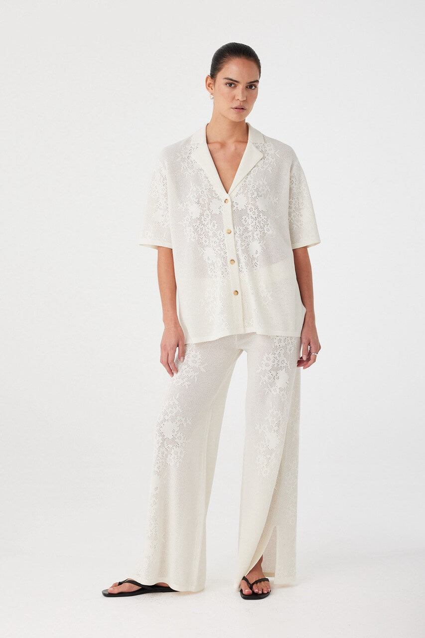 Cream crochet shirt styled with matching pants, viewed diagonally. Relaxed tailoring meets elevated texture for trans-seasonal layering.