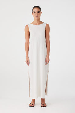 Model wears sleeveless cream knit maxi dress with a high boat neckline and soft side slits, crafted in a breathable linen–cotton blend for warm-weather ease.