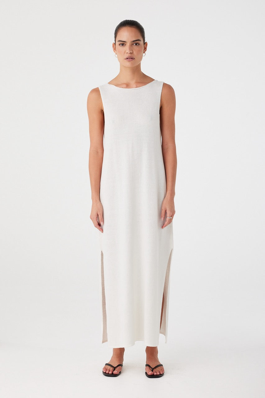 Model wears sleeveless cream knit maxi dress with a high boat neckline and soft side slits, crafted in a breathable linen–cotton blend for warm-weather ease.