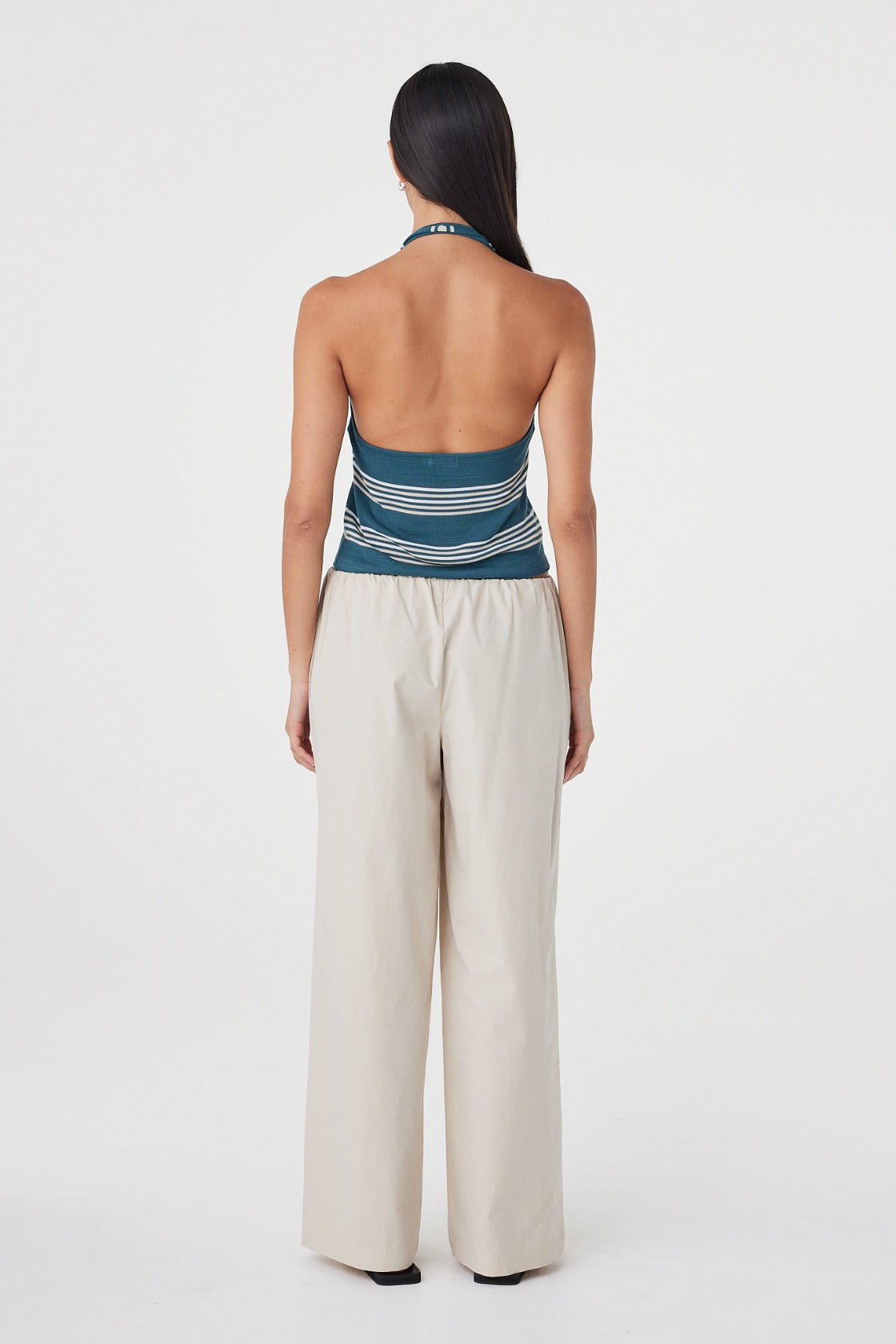 Back view of the Annika Pant in Taupe styled with a striped tank, showing the clean waistband finish and relaxed drape.
