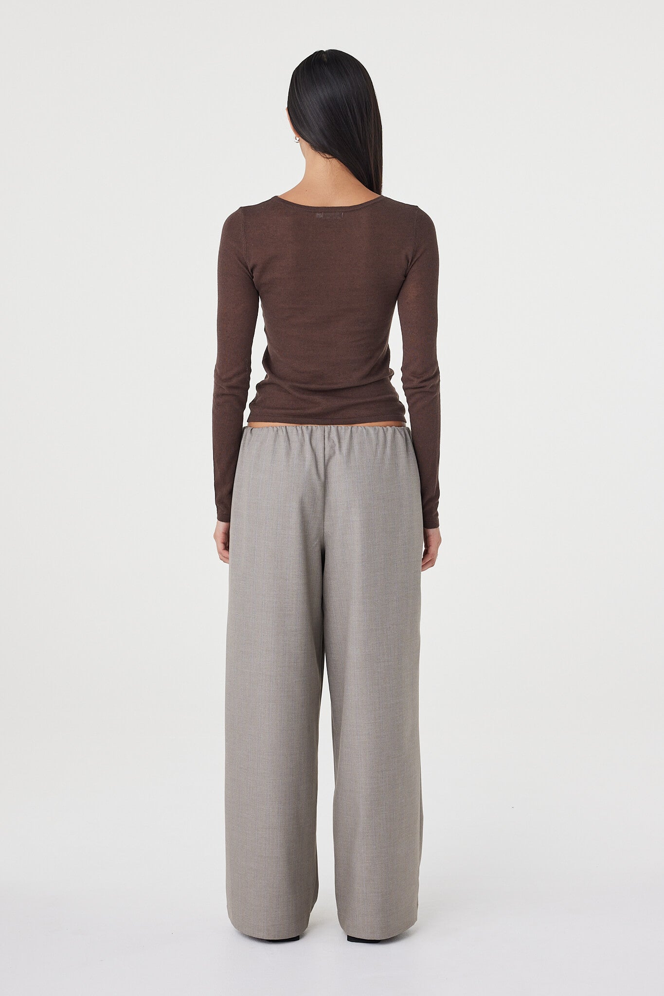 Back view of the Aston LS Top in espresso featuring the slim fit shape, lightweight knit texture and long sleeve design paired with relaxed taupe pants