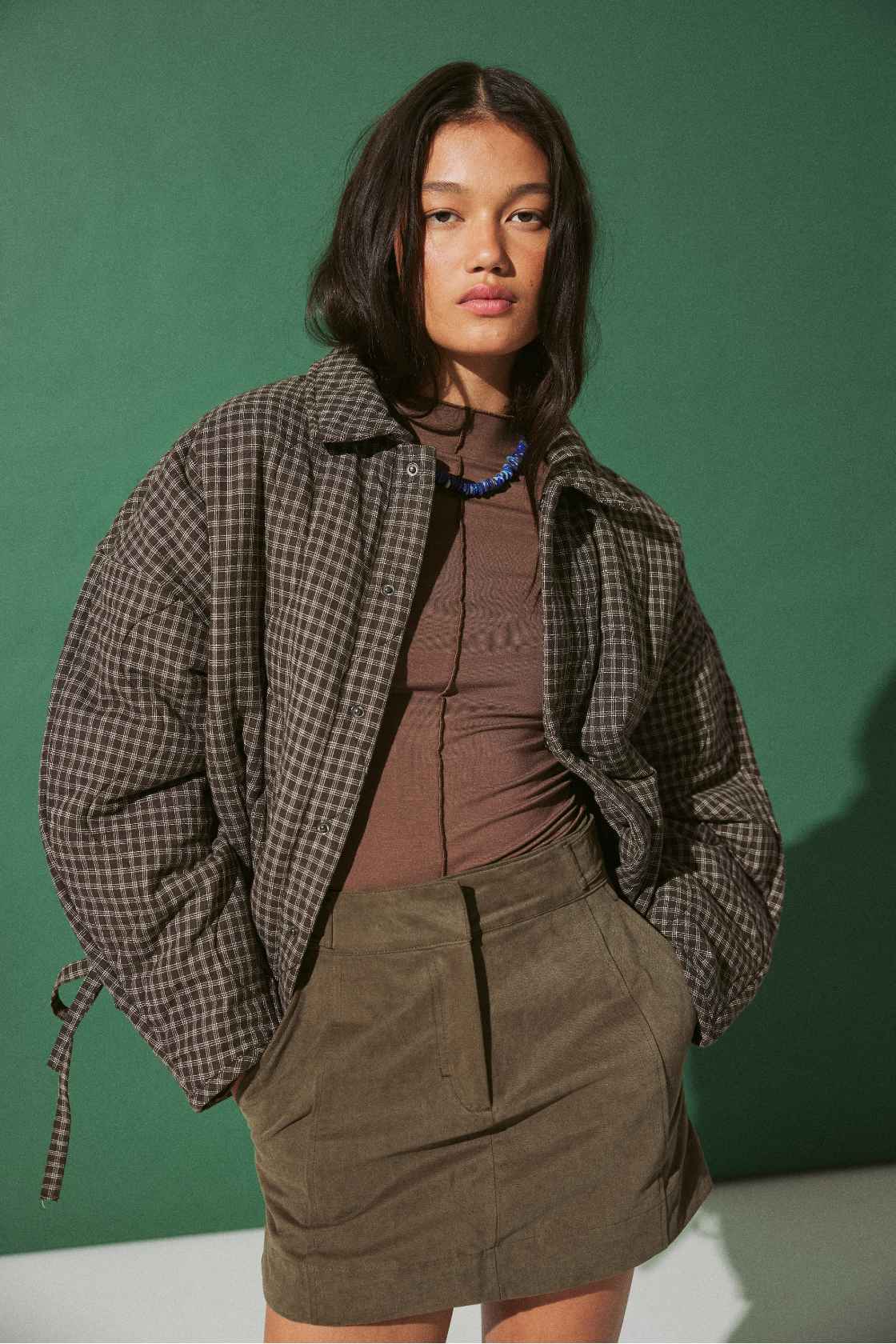Model wearing Espresso Check quilted cotton jacket with slouchy cocoon fit, styled over khaki mini skirt for cool evenings