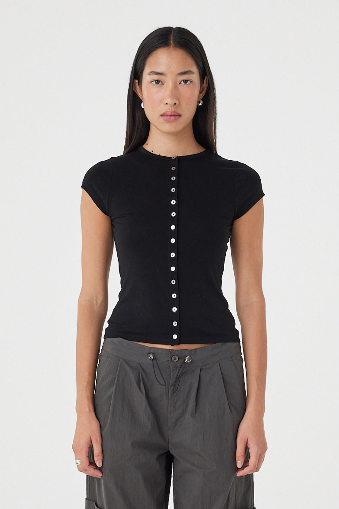 Front view of the Robbie Top in Black featuring a slim fit, centre front button closure and cap sleeves, styled with charcoal utility pants.
