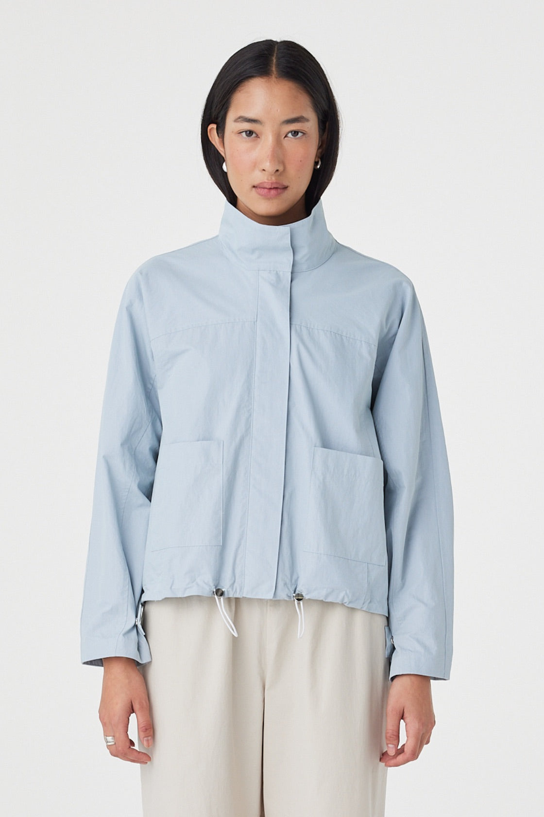 Front view of the Addie Jacket in Pale Blue featuring a funnel neckline, concealed zip closure and oversized front patch pockets, styled with wide-leg trousers.