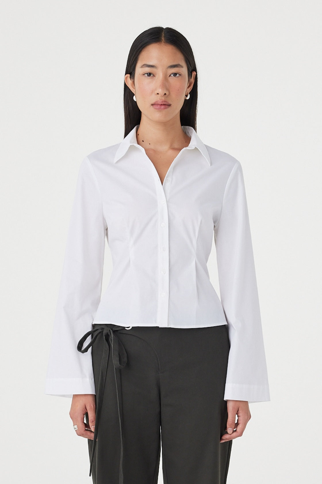 Front view of the Ari Shirt in White featuring a fitted silhouette, collared neckline and concealed button closure, styled with charcoal wrap-detail trousers.