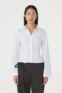 Front view of the Ari Shirt in White featuring a fitted silhouette, collared neckline and concealed button closure, styled with charcoal wrap-detail trousers.