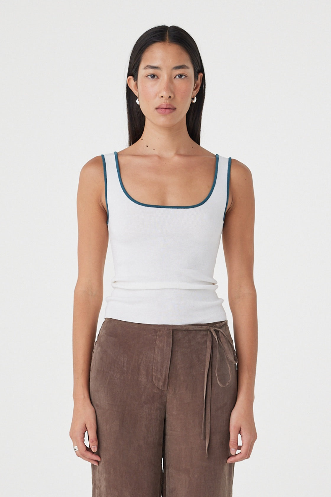 Front view of the Kaya Tank in Cream & Teal featuring a slim fit, scoop neckline and contrast teal edging, styled with brown pants.