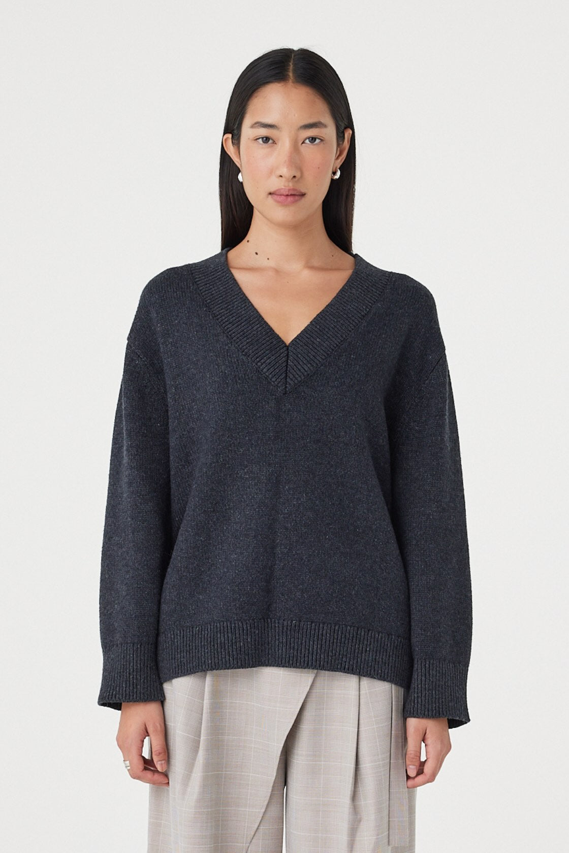 Front view of the Zenya Sweater in Dark Grey Marle featuring a deep V-neckline, soft marled knit texture and relaxed silhouette, styled with light grey wide-leg trousers.