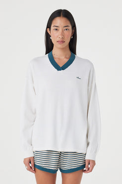 Front view of the Cammy LS Tee in Cream & Teal featuring a contrast ribbed V-neckline, embroidered logo and oversized silhouette, styled with striped shorts.