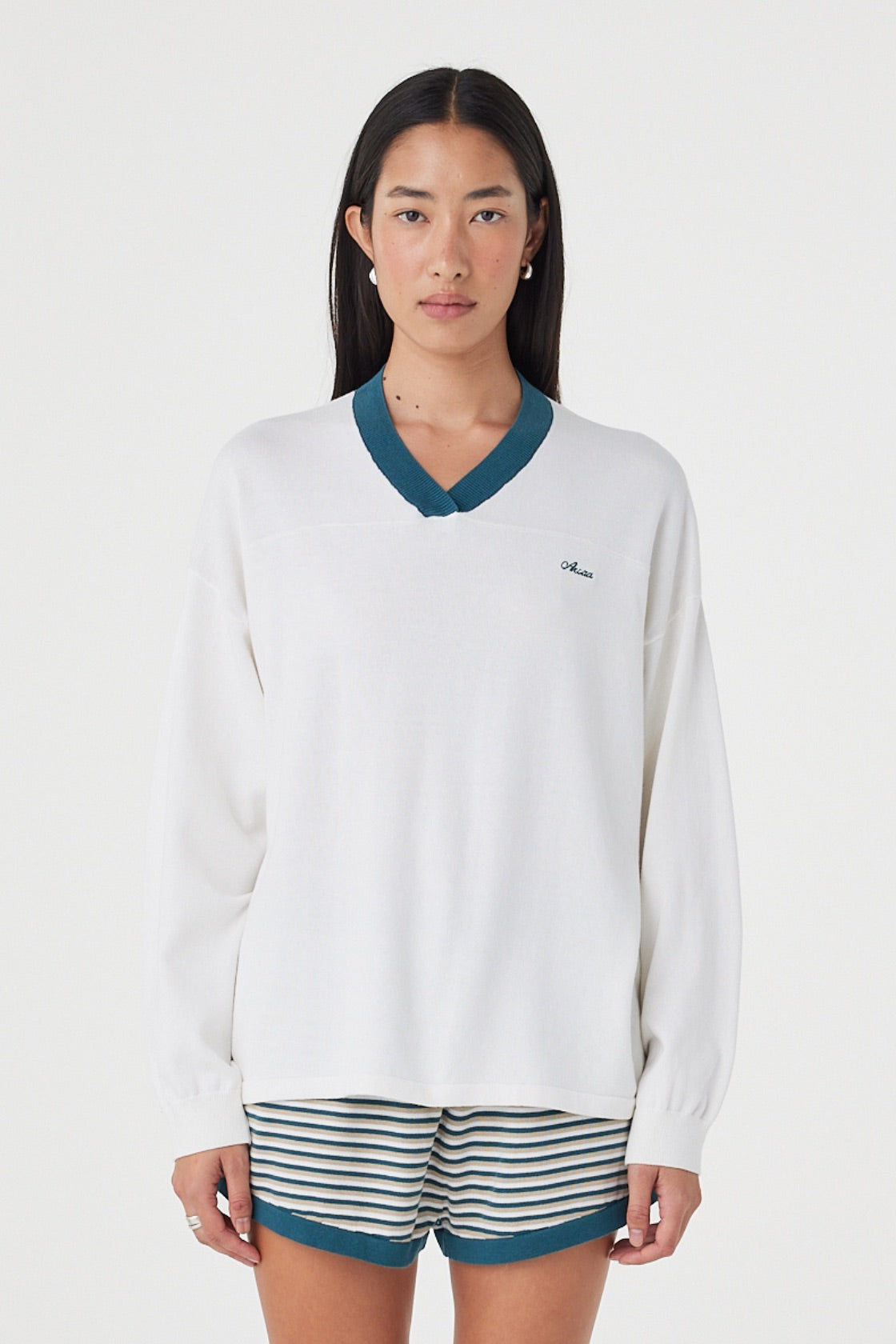 Front view of the Cammy LS Tee in Cream & Teal featuring a contrast ribbed V-neckline, embroidered logo and oversized silhouette, styled with striped shorts.