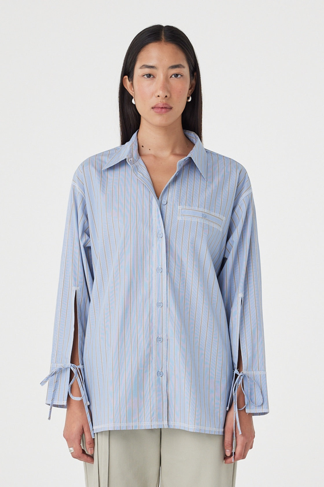 Front view of the Blair Shirt in Blue Taupe Stripe featuring the relaxed silhouette, adjustable waist tie, oversized cuff ties and contrast overlocking, styled with light sage trousers.